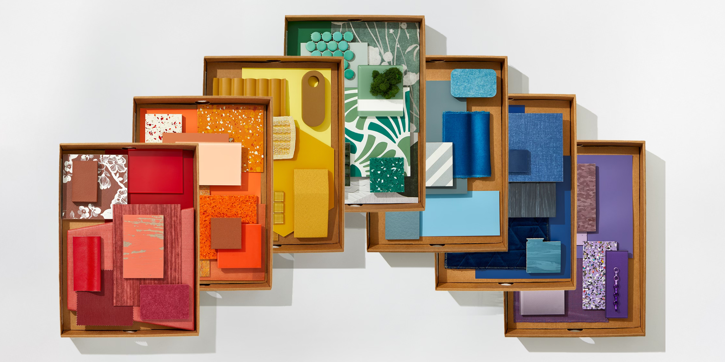 A flatlay image of boxed colorful textiles, stone, wallpaper, and materials.