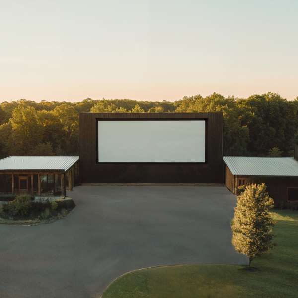 A modern drive-in movie theater with natural landscaping, wood paneled buildings, and smooth concrete parking lots.