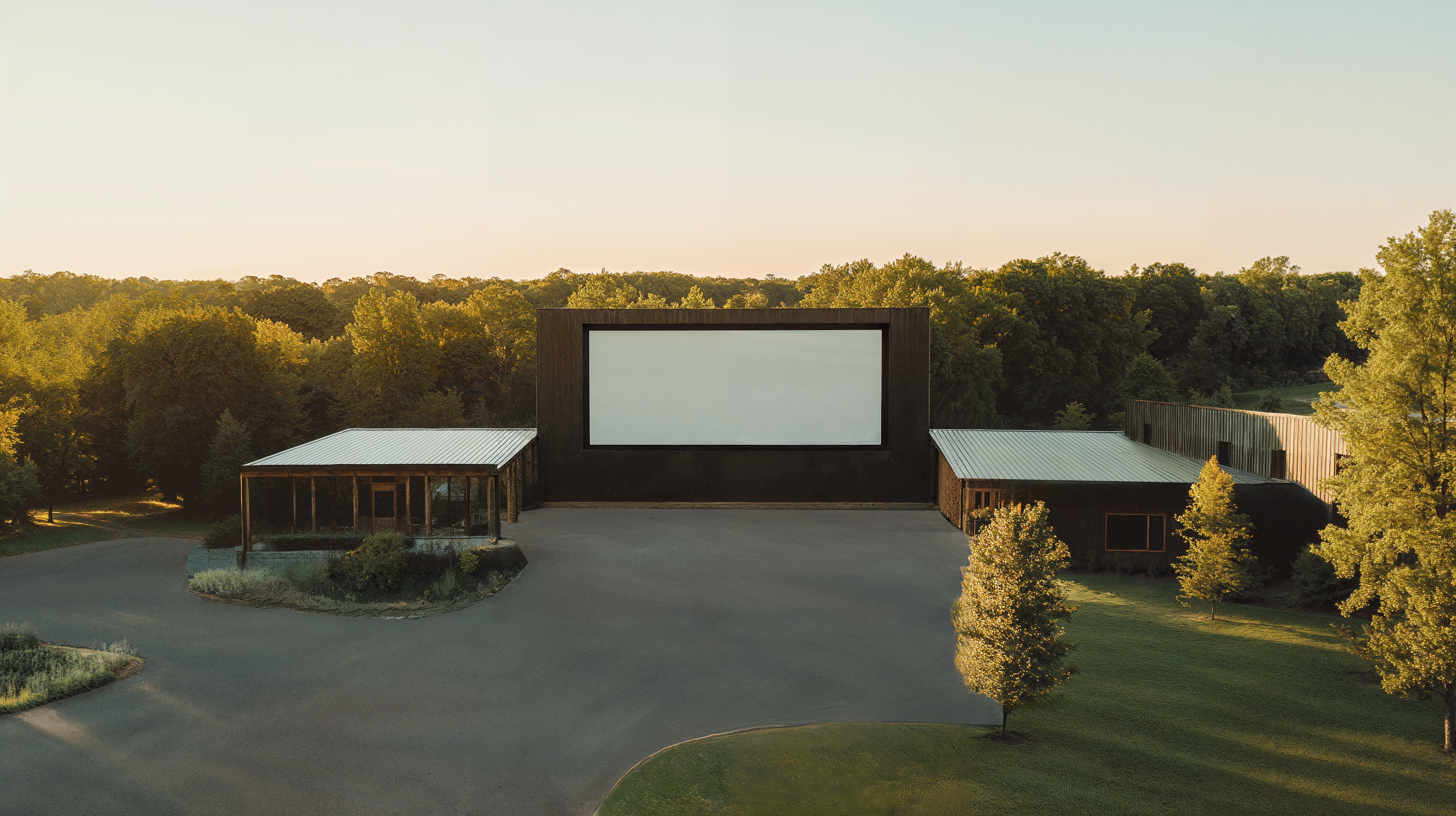 A modern drive-in movie theater with natural landscaping, wood paneled buildings, and smooth concrete parking lots.