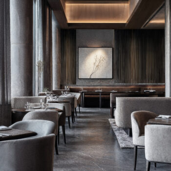 An interior dining room with dark wood floors, gray drapery, and silver finishes.