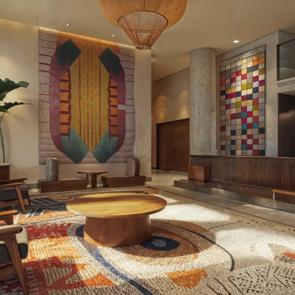 A hotel lobby that makes a bold impression with pattern area rug and tapestries hanginf on the walls. Two gray and wood chairs sit around a wooden coffee table with stone and marble floors and accents.