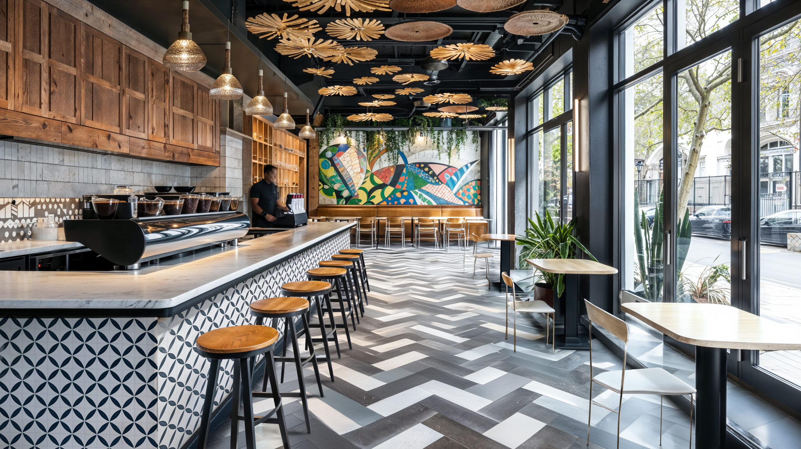 A coffee shop with black, white and gray patterned floors, a coffee bar and table seating around the rest of the room.