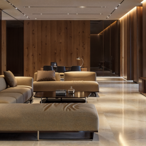 A hotel lounge with wood paneling on the walls in a contemporary design with tan couches and light beige tile floors.