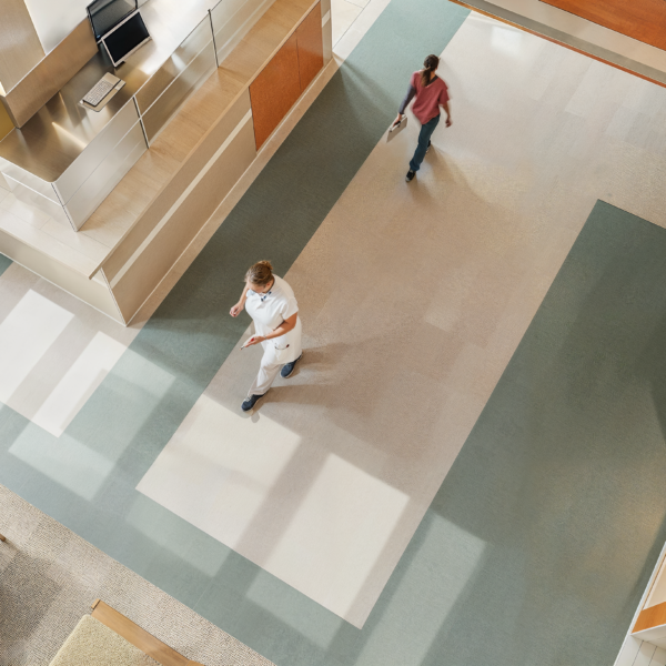 Aerial shot of a healthcare facility with Anti-Fatigue Flooring and windows letting in light as people pass each other in a hallway.