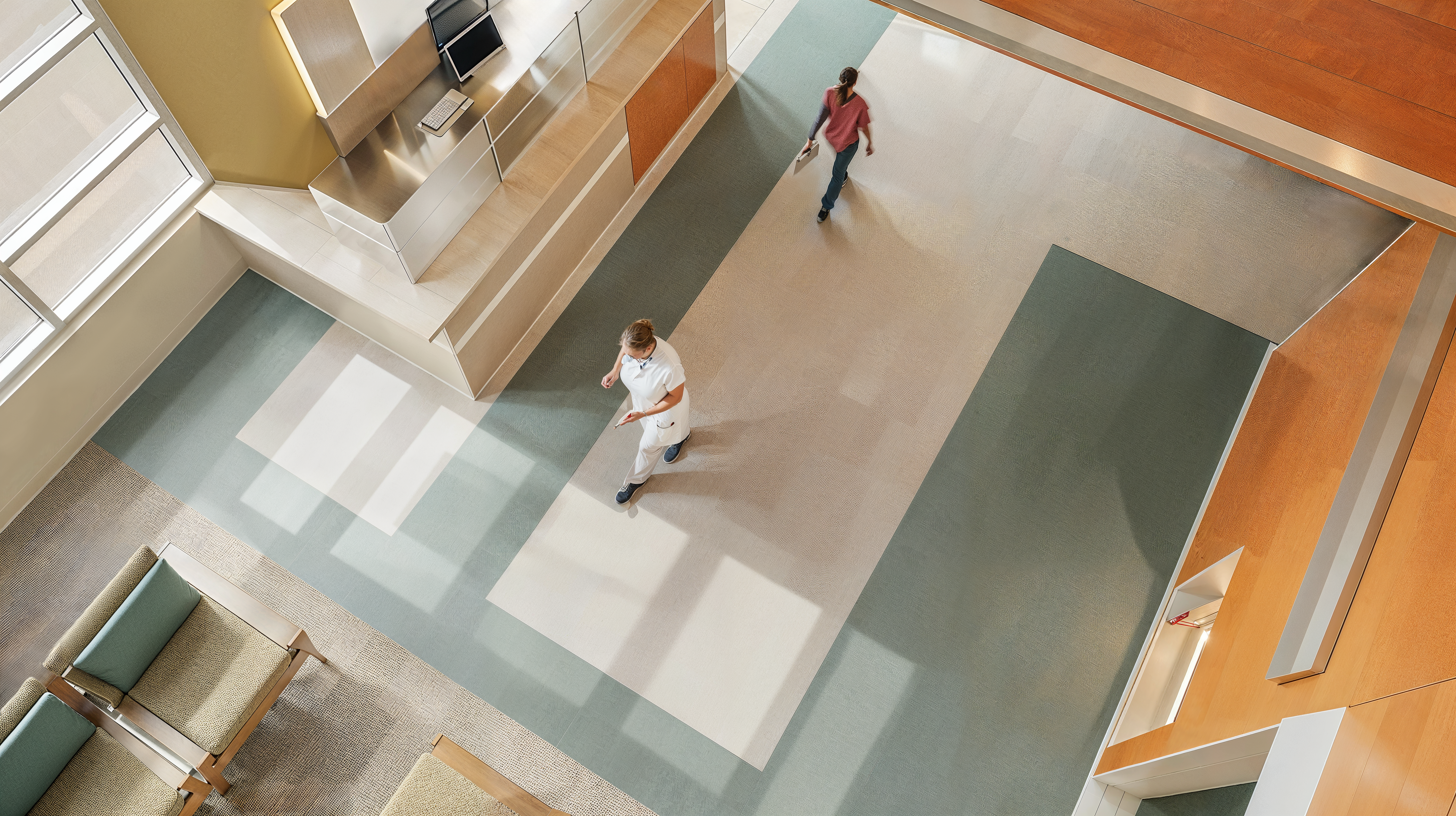 Aerial shot of a healthcare facility with Anti-Fatigue Flooring and windows letting in light as people pass each other in a hallway.