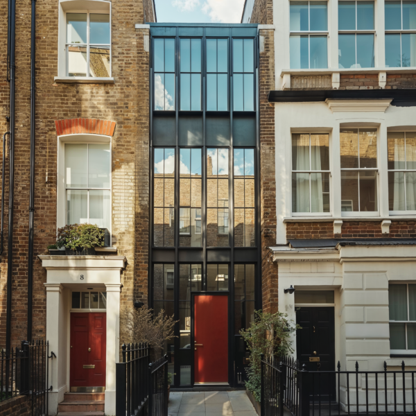 A row of skinny townhouses. The one on the far left is made of faded red brick, the center house is made of steel and glass and the home on the right is white brick.