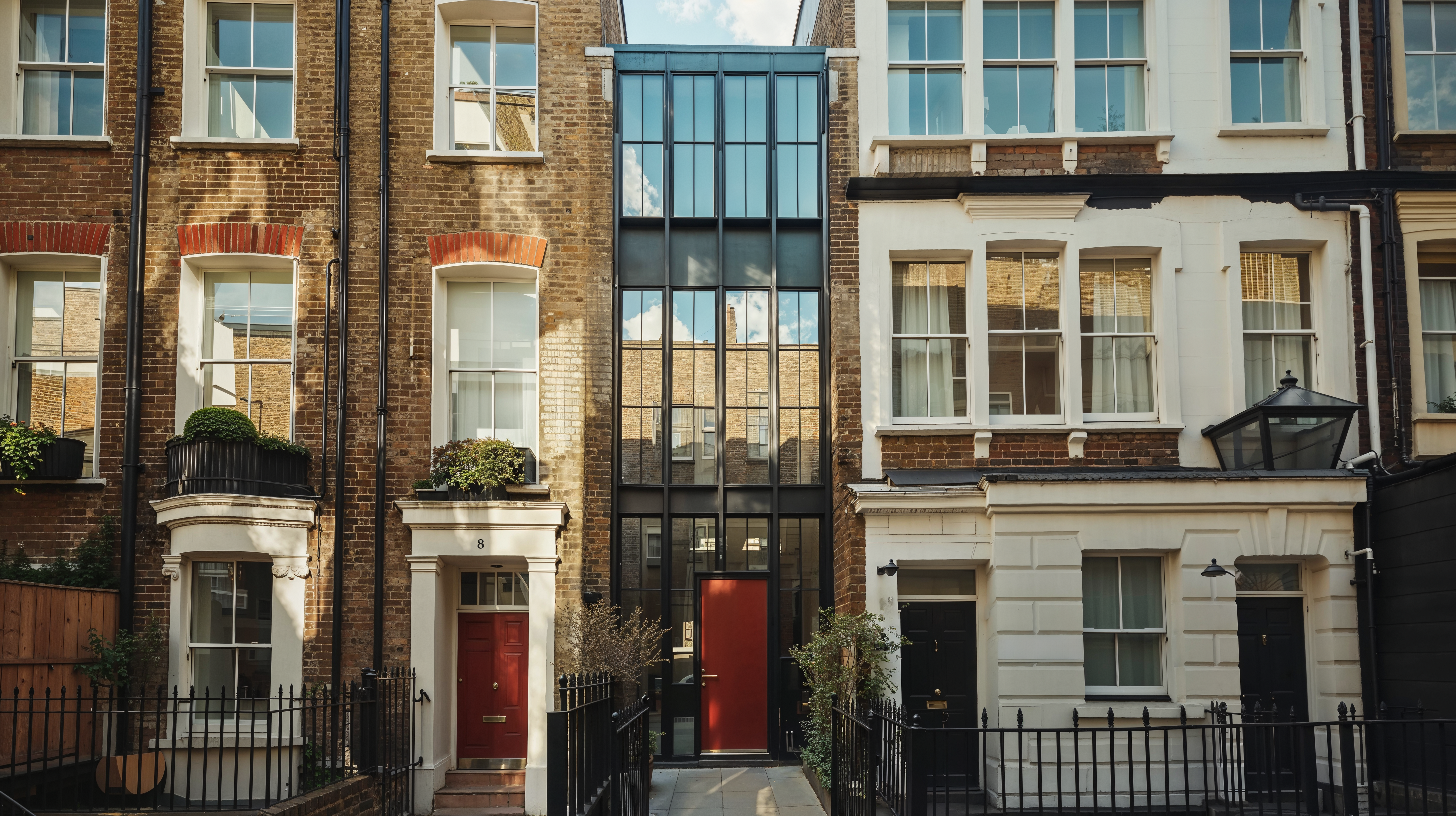 A row of skinny townhouses. The one on the far left is made of faded red brick, the center house is made of steel and glass and the home on the right is white brick.