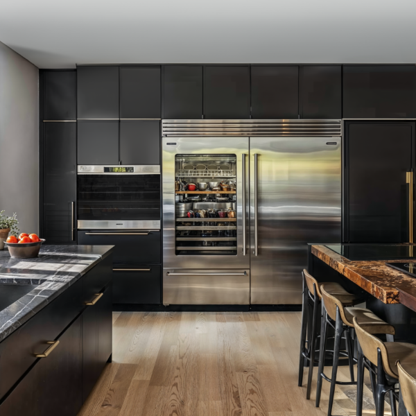 A gourmet kitchen with wood floors, gray and white marble counter tops around sink facing windows to the outside. Stainless steel refrigerator and oven.