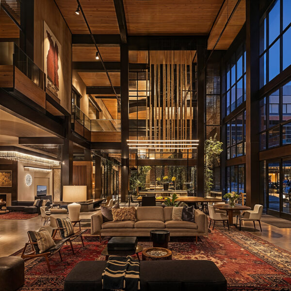 Natural Materials in Mixed-Use Residential Design lobby with wood paneling on the walls and ceilings, floor to ceiling windows, various seating areas with neutral color upholstery and muted red tone area rugs.