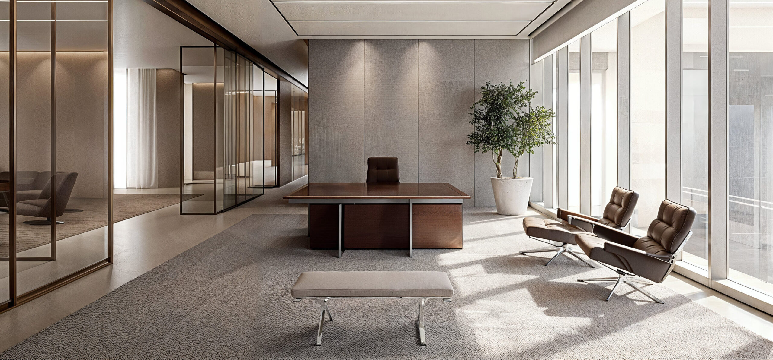 A neutral tone office space with beige floors with large area rugs and tile. A large wooden desk with dark brown leather chairs 2 in the room and one behind the desk.