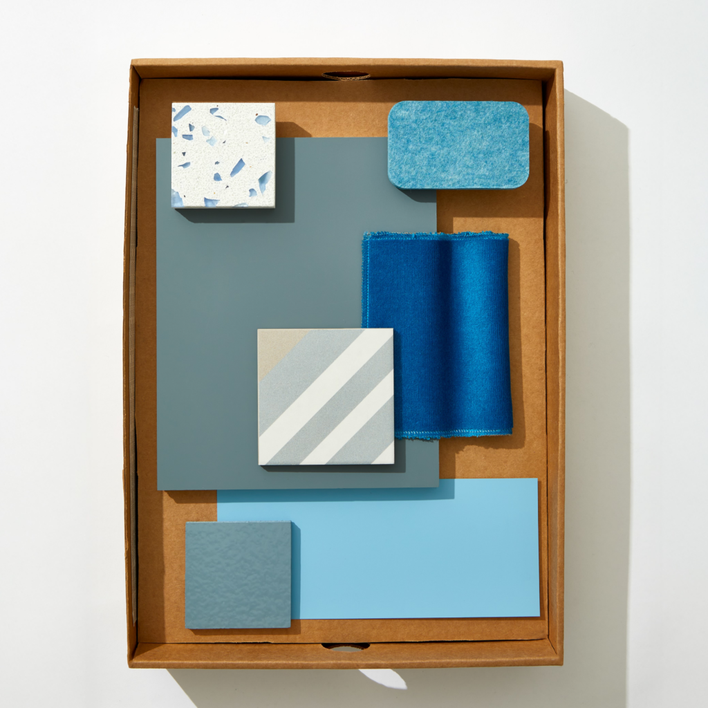 A flatlay image of boxed blue textiles, stone, wallpaper, and materials.