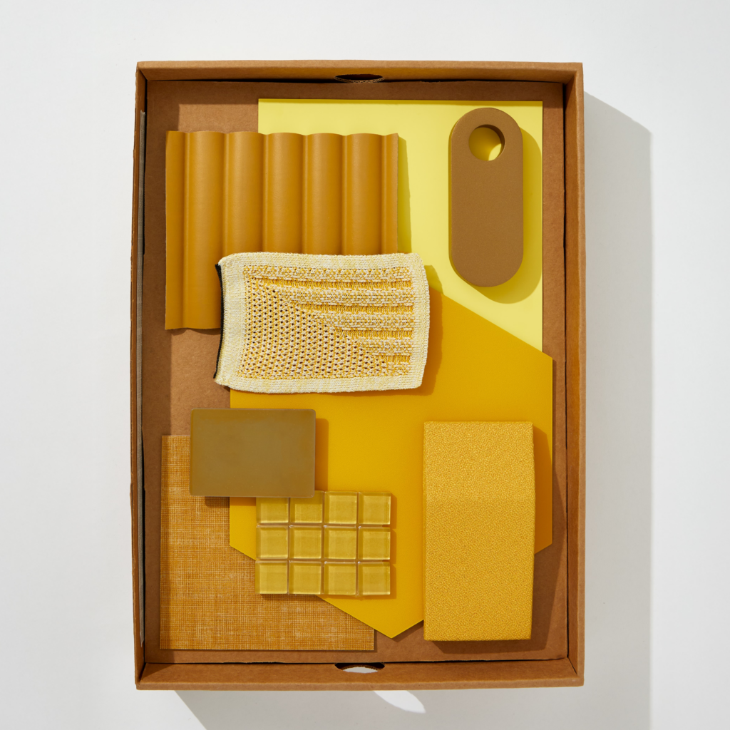 A flatlay image of boxed yellow textiles, stone, wallpaper, and materials.