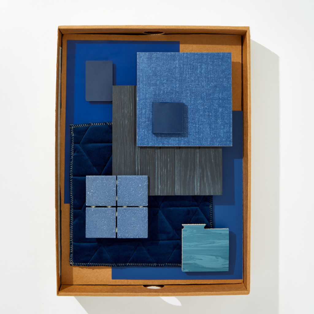 A flatlay image of boxed dark blue textiles, stone, wallpaper, and materials.