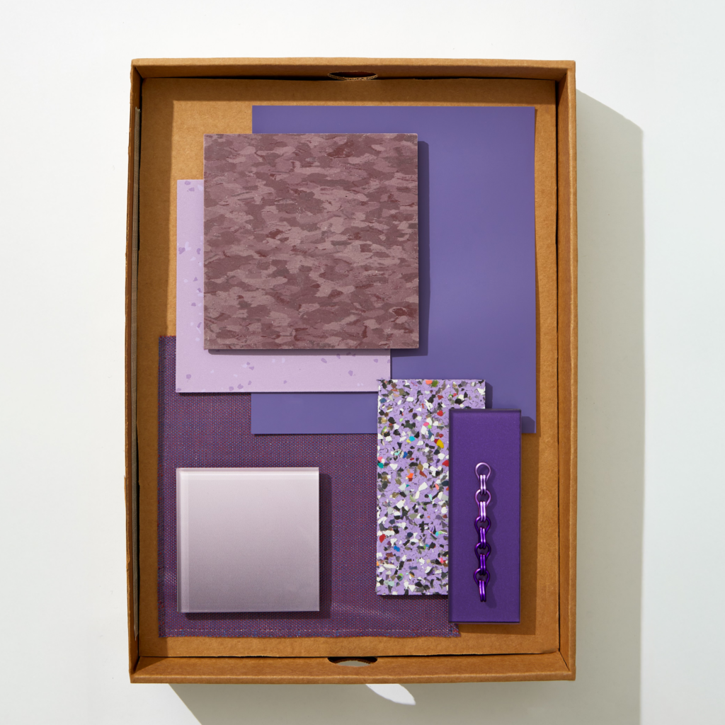 A flatlay image of boxed purple textiles, stone, wallpaper, and materials.