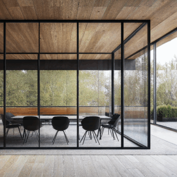A Norwegian cabin designed workplace with wood paneled ceilings, large windows, and grey carpets.