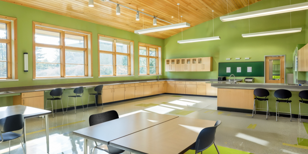 Sustainable high school interior of a lab classroom with green walls, wood paneled ceilings, bright open windows letting in lots of natural light. 