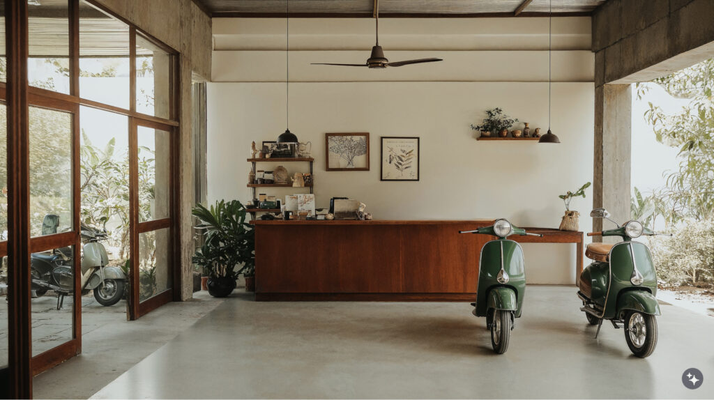 Balinese design scooter rental with concrete floors, wooden desk, wooden door and windows. The walls are a cream color with views on both sides of the room to the outside. 