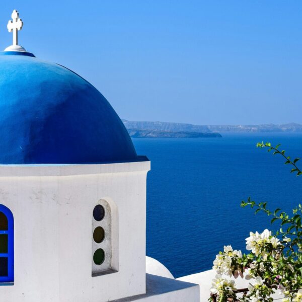 A photograph of Santorini Design featuring a domed building with a vibrant blue roof and door and crisp while building. Overlooking the sea.