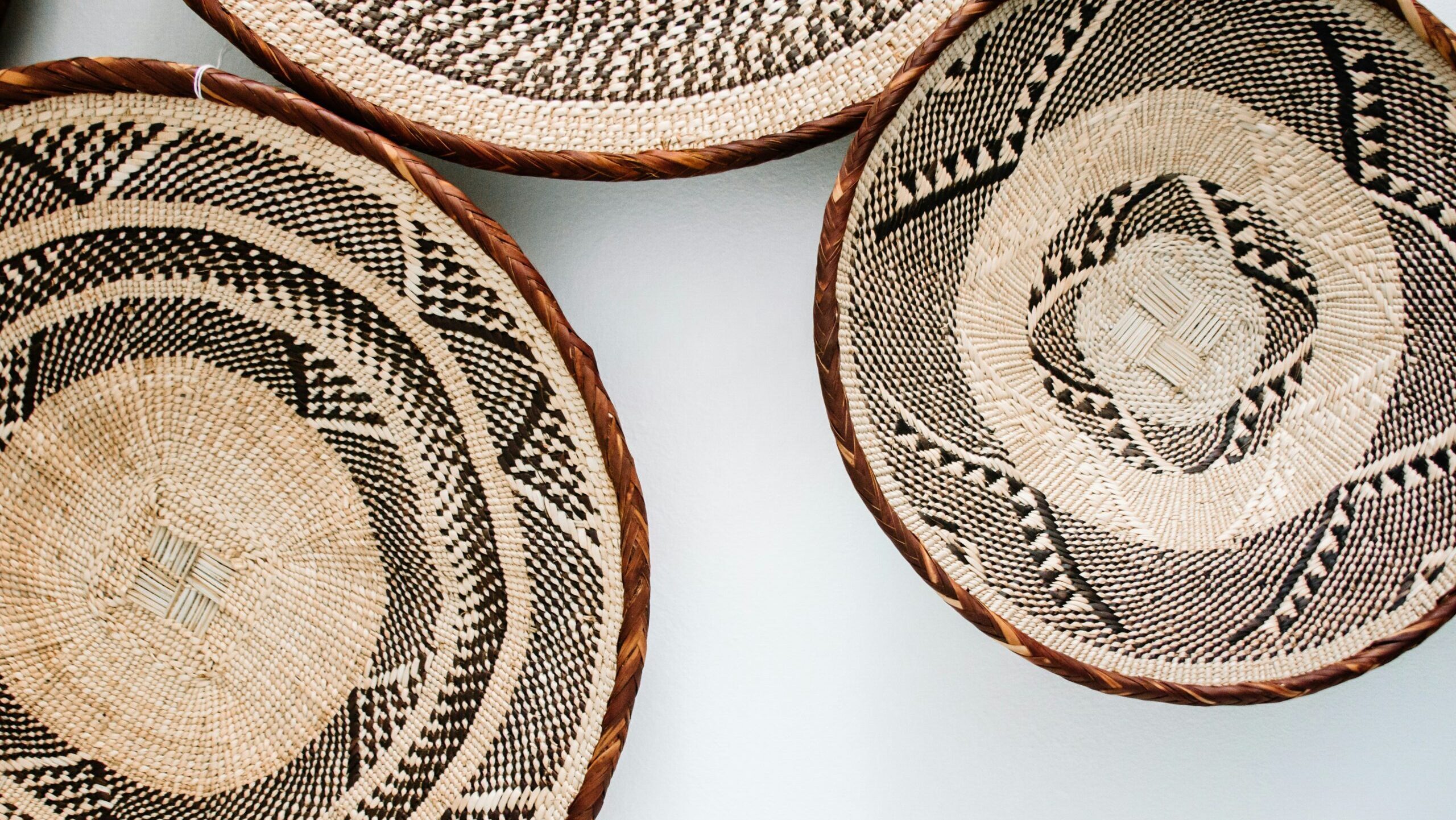 A closeup of three woven baskets with geometric patterns, arranged on a white background. The basket designs feature intricate black and brown designs that create visual interest and depth.