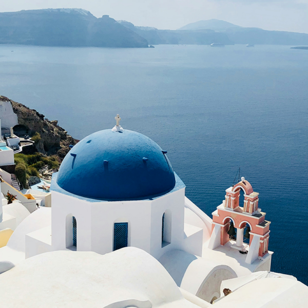 Photograph of Santorini, Greece with white buildings and blue domes overlooking the sea, with small church in foreground