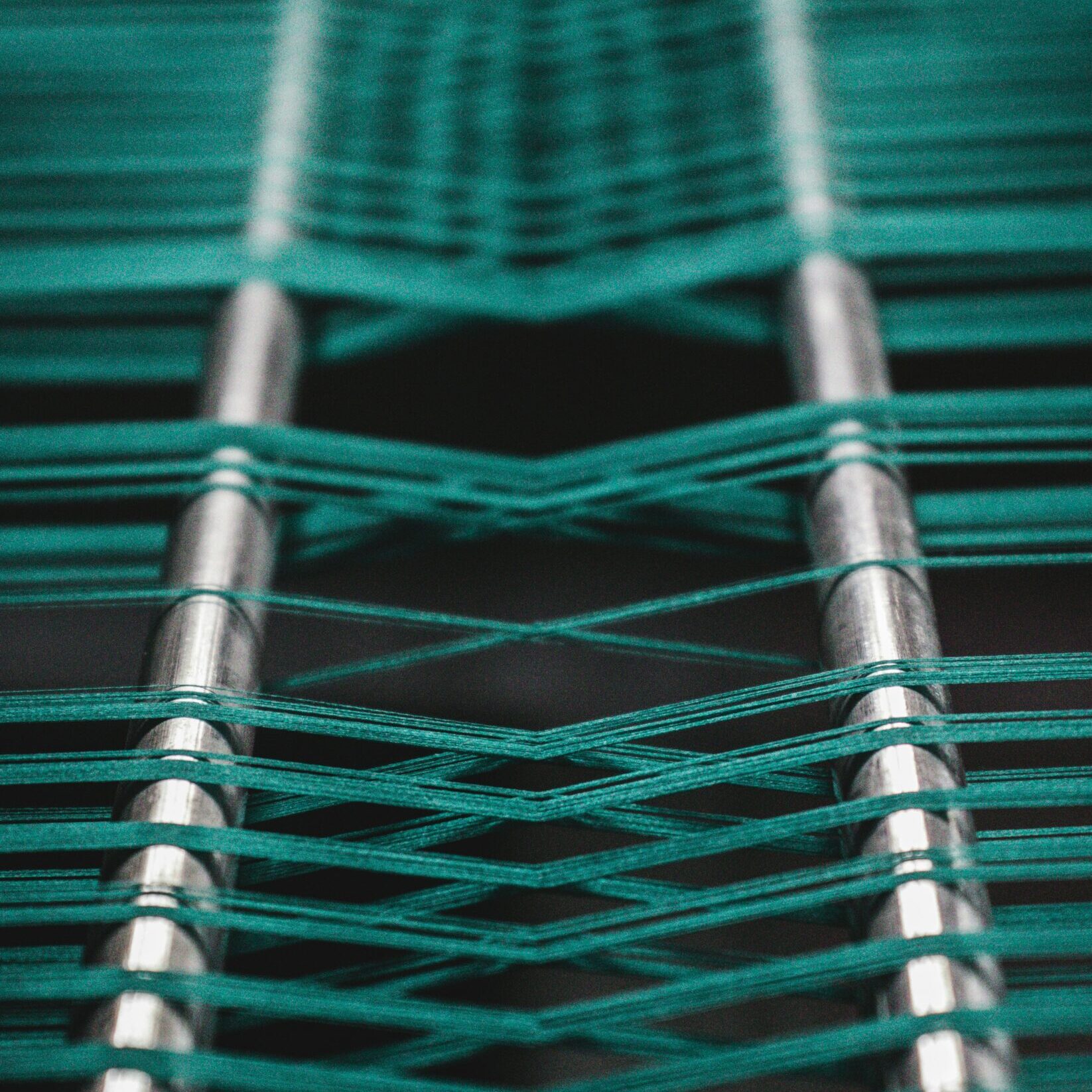 A macro shot of green threads being woven on an industrial loom, capturing the intricate details and textures in high resolution detail