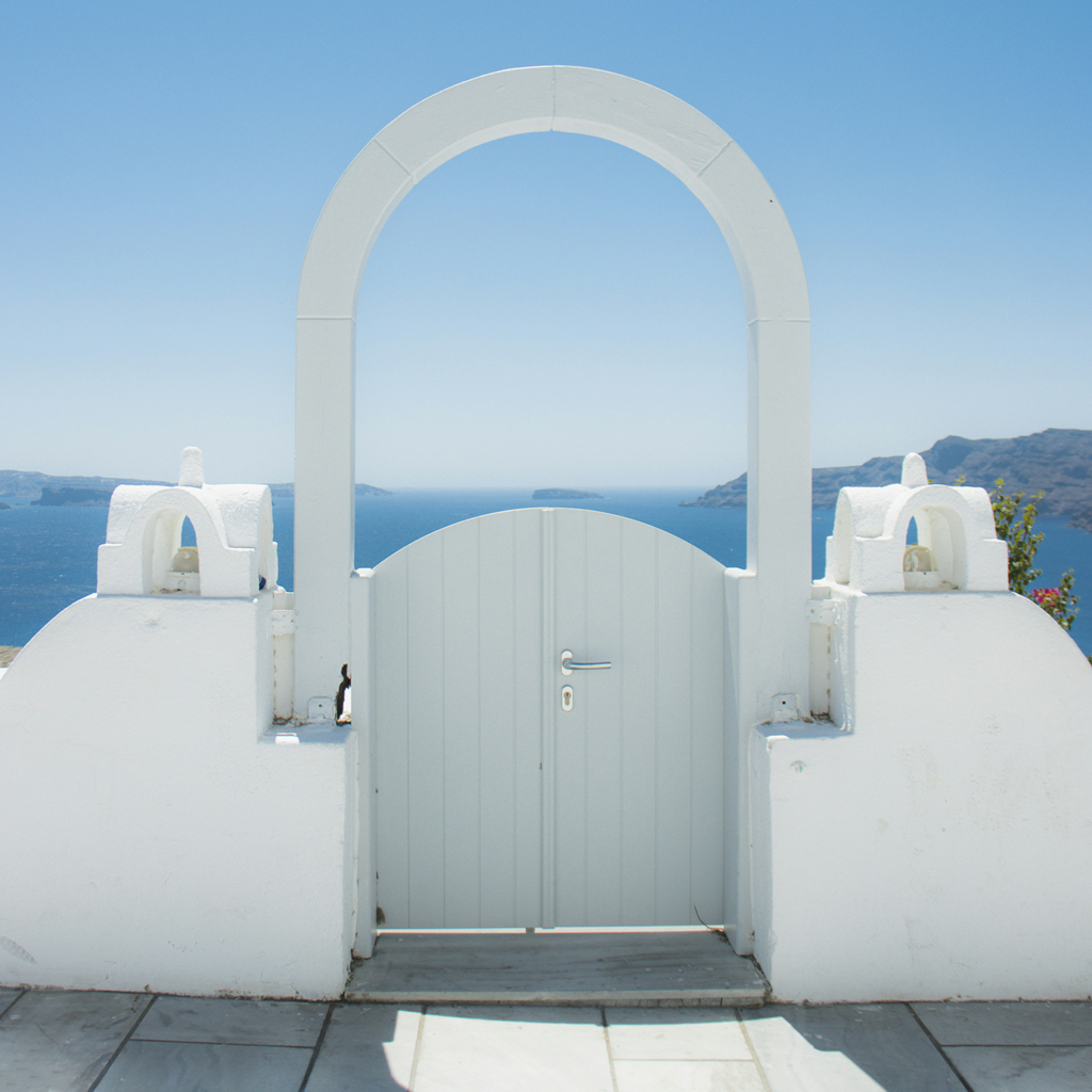 A white arched gate leading to the ocean, white Greek-style architecture, blue sky.