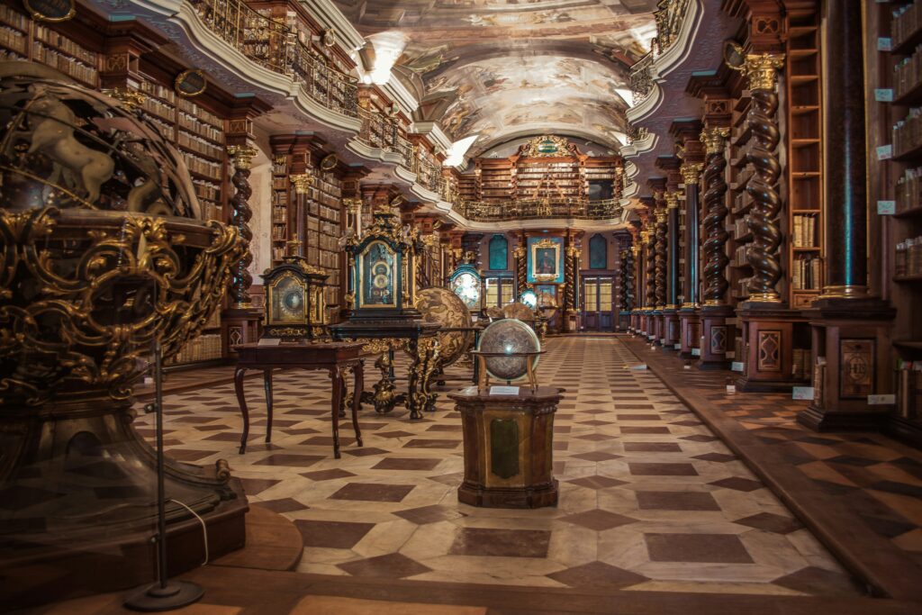 A library in Prague highlighting science, geometry and astronomy from 1700. Books lining the walls of a room with brown and biege tiled floors with several ornately carved wood tables and globes in the center of the room. 