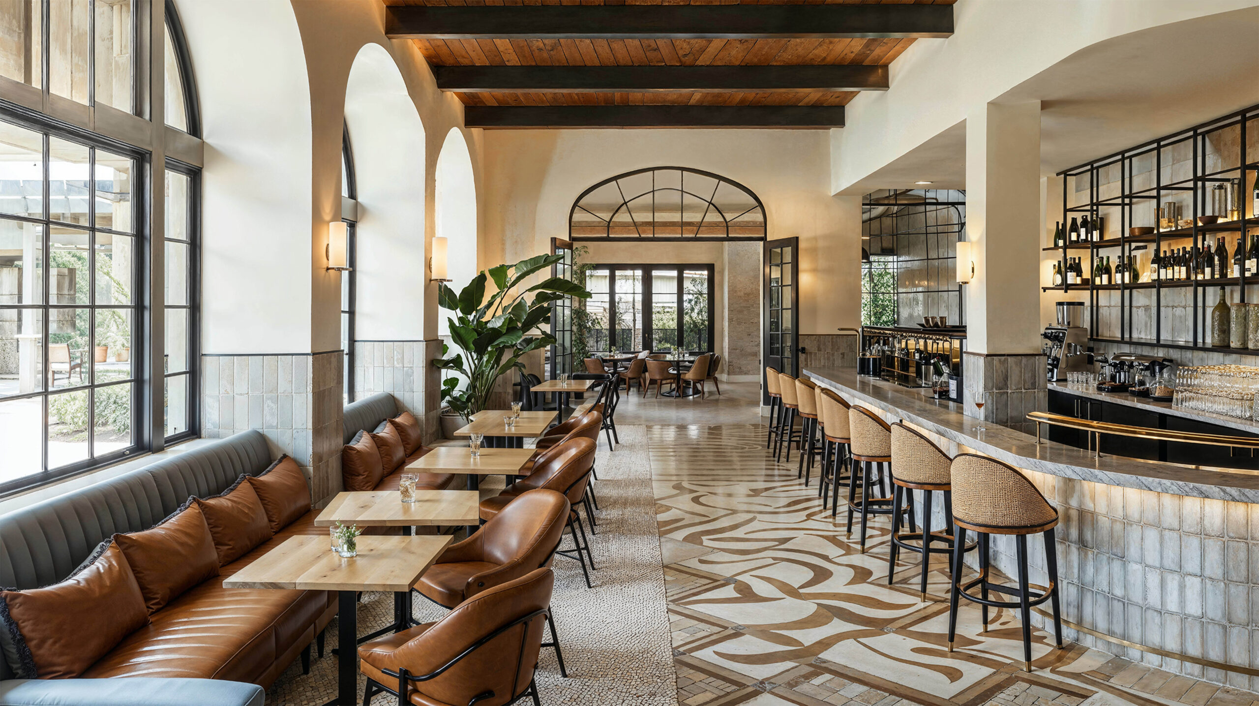 A restaurant showcase tile and stone in hospitality design with beige and brown abstract pattern tile on part of the floor and small beige mosaic stone on another. A gray natural stone countertop at the bar with small tables sitting across from it.