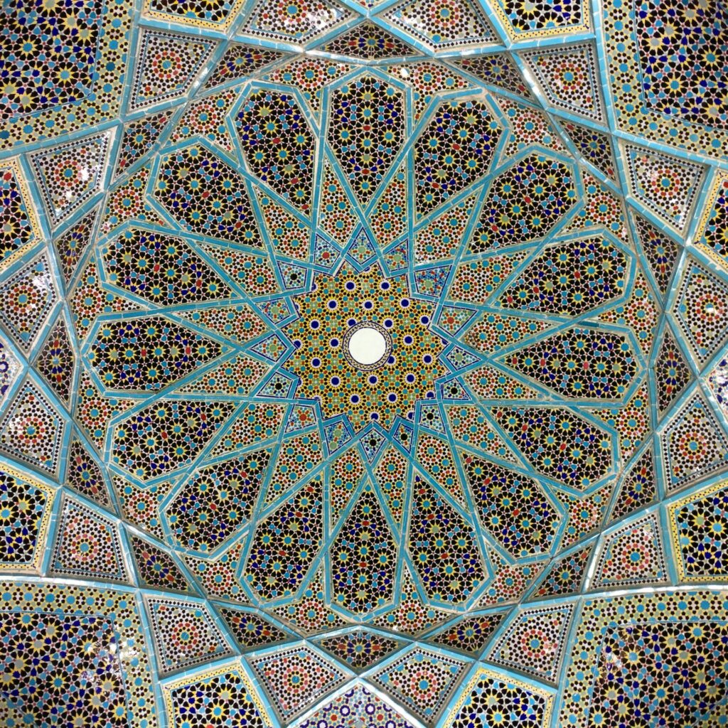 A closeup shot of the intricate geometric patterns on a dome ceiling, showcasing its vibrant colors and detailed mosaic work in turquoise blue and red hues. The delicate designs create symmetrical shapes that form beautiful circular structures adding depth to the space. This composition captures the beauty of arabesque design with a focus on ornate decorative elements.