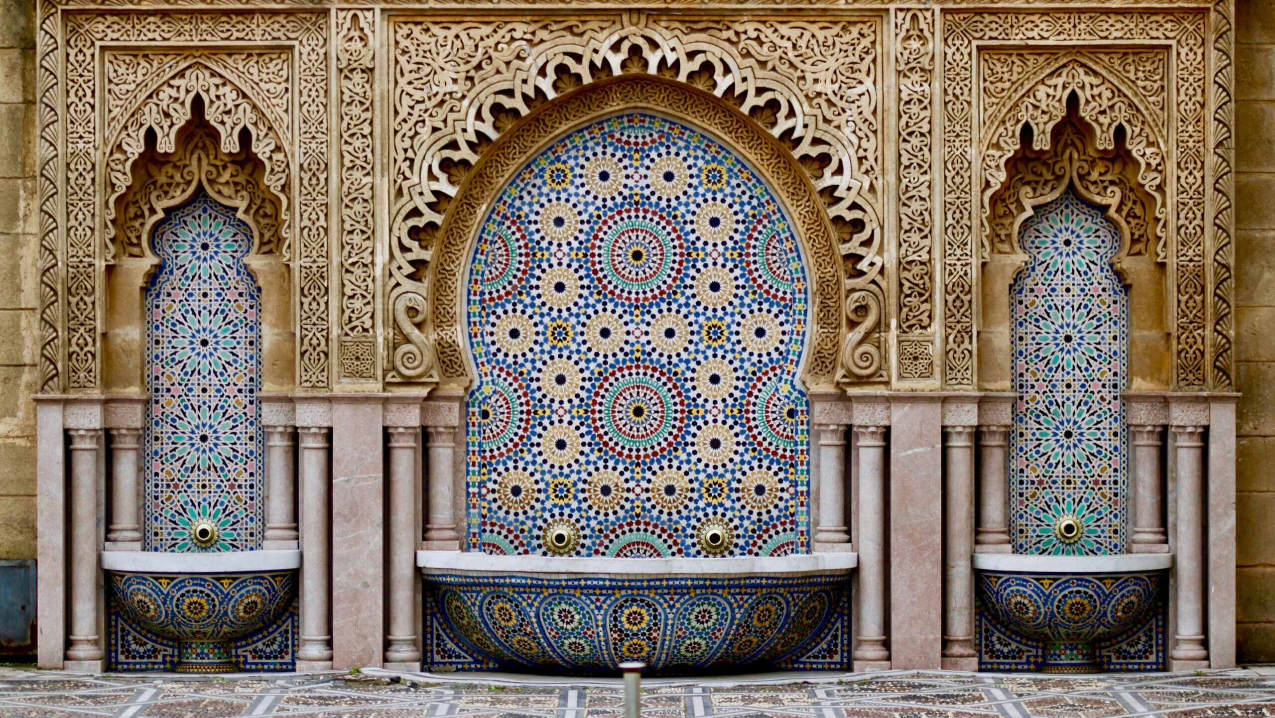 A courtyard designed in arabesque patterned tile with a decorative fountain in the middle.