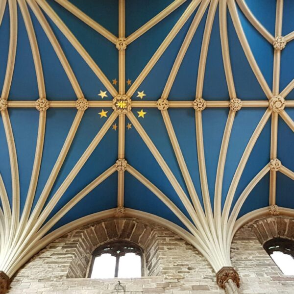 A photo of a transcendent ceiling in the color blue and gold with stars, showing arches with vaults on top. In the style of gothic architecture with arched windows just below the ceiling.