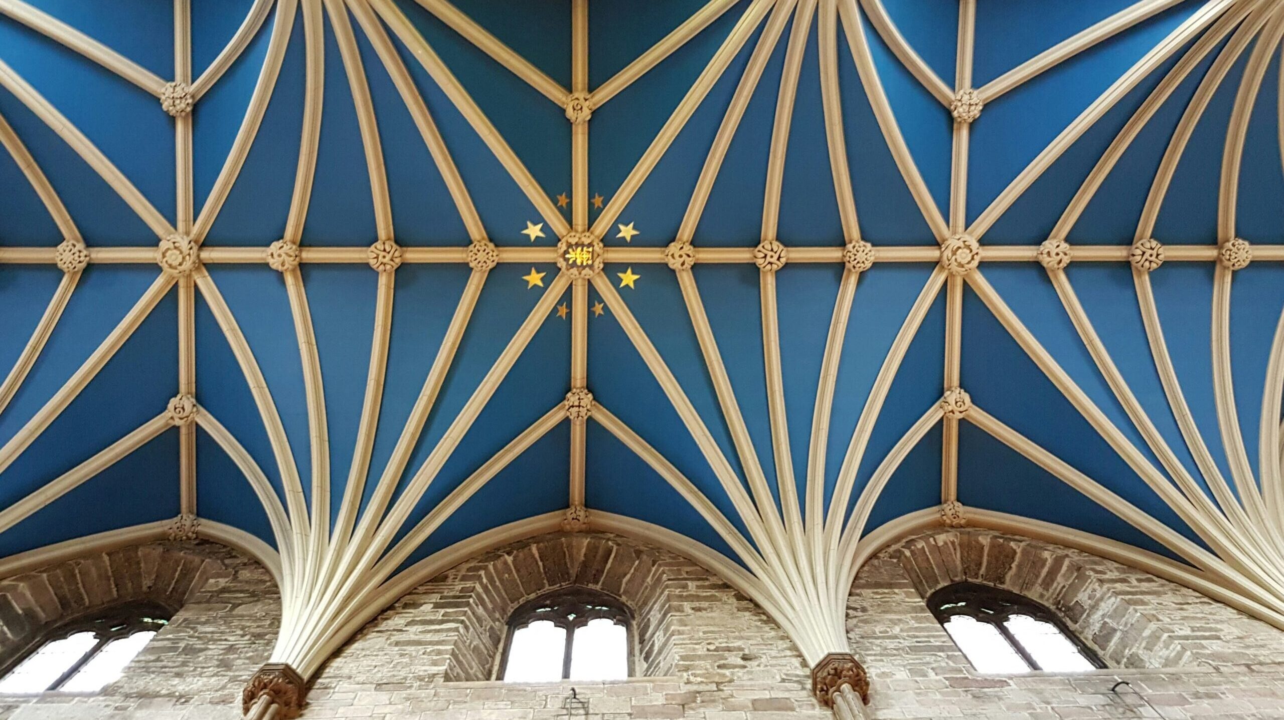 A photo of a transcendent ceiling in the color blue and gold with stars, showing arches with vaults on top. In the style of gothic architecture with arched windows just below the ceiling.