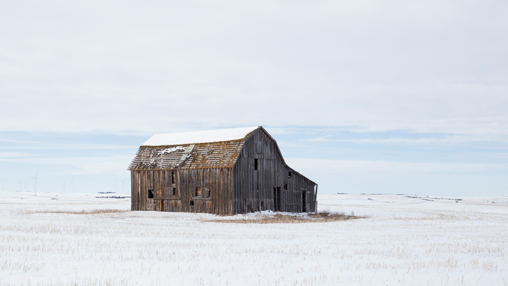 An old abandoned barn sitting in the distance in a snowy prairie landscape. 