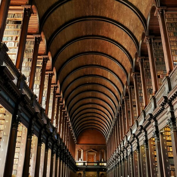 A photograph inside the Library of Trinity College in Dublin Ireland looking up at the second floor and ornate ceiling.