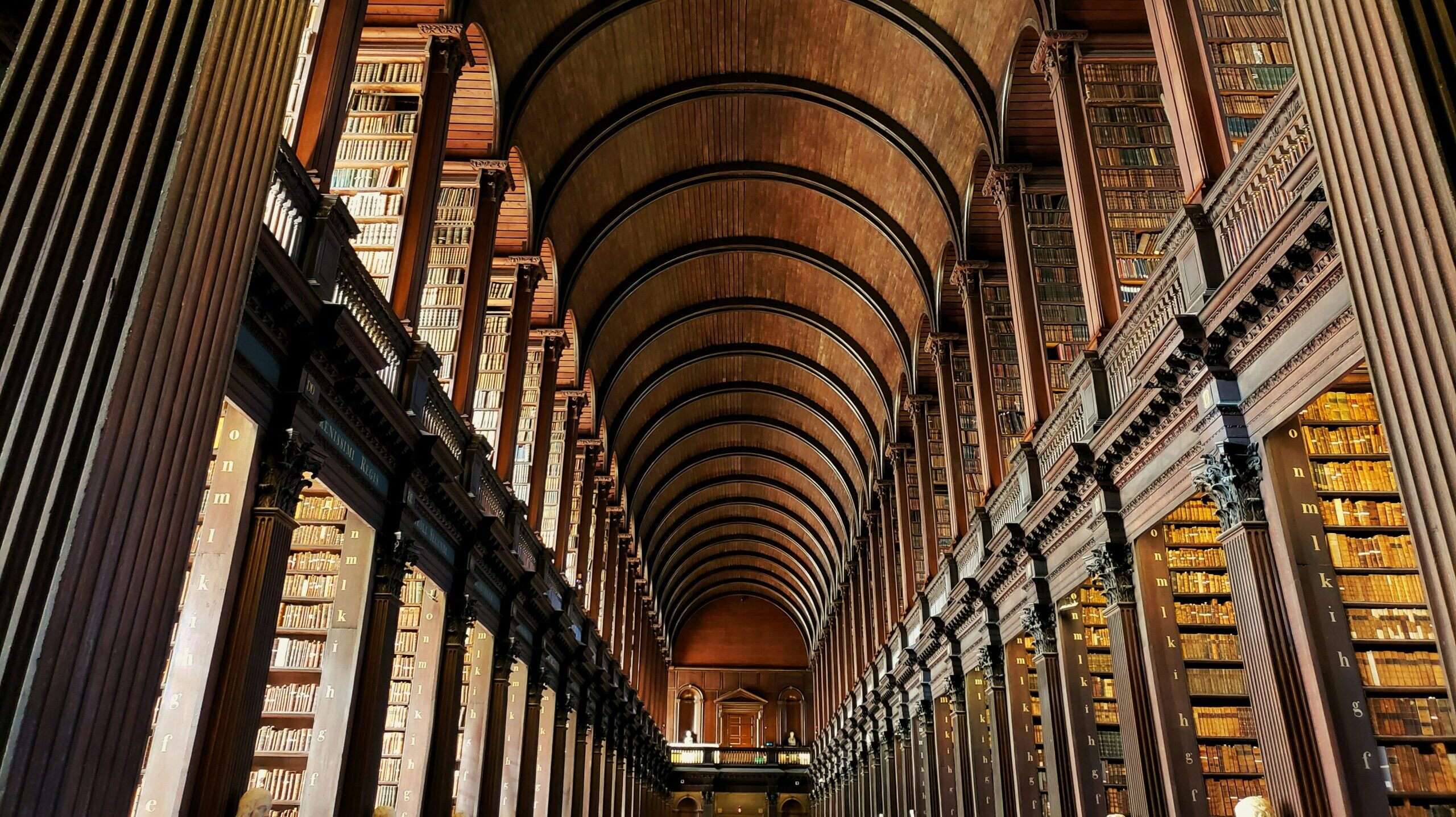 A photograph inside the Library of Trinity College in Dublin Ireland looking up at the second floor and ornate ceiling.