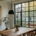 Dutch canal house dining table area with a wood table and chairs, plants, paneled windows, pendant lighting, and artwork.