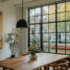 Dutch canal house dining table area with a wood table and chairs, plants, paneled windows, pendant lighting, and artwork.