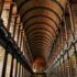 A photograph inside the Library of Trinity College in Dublin Ireland looking up at the second floor and ornate ceiling.