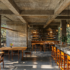 A restaurant with concrete floors, walls, ceilings and countertops, softened by wooden seats and tables.