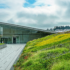 Green roofs and walls on top of an urban building. A walkway surrounded on both sides by concrete and steel retention walls line both sides surrounded by a variety of plants and flowers.